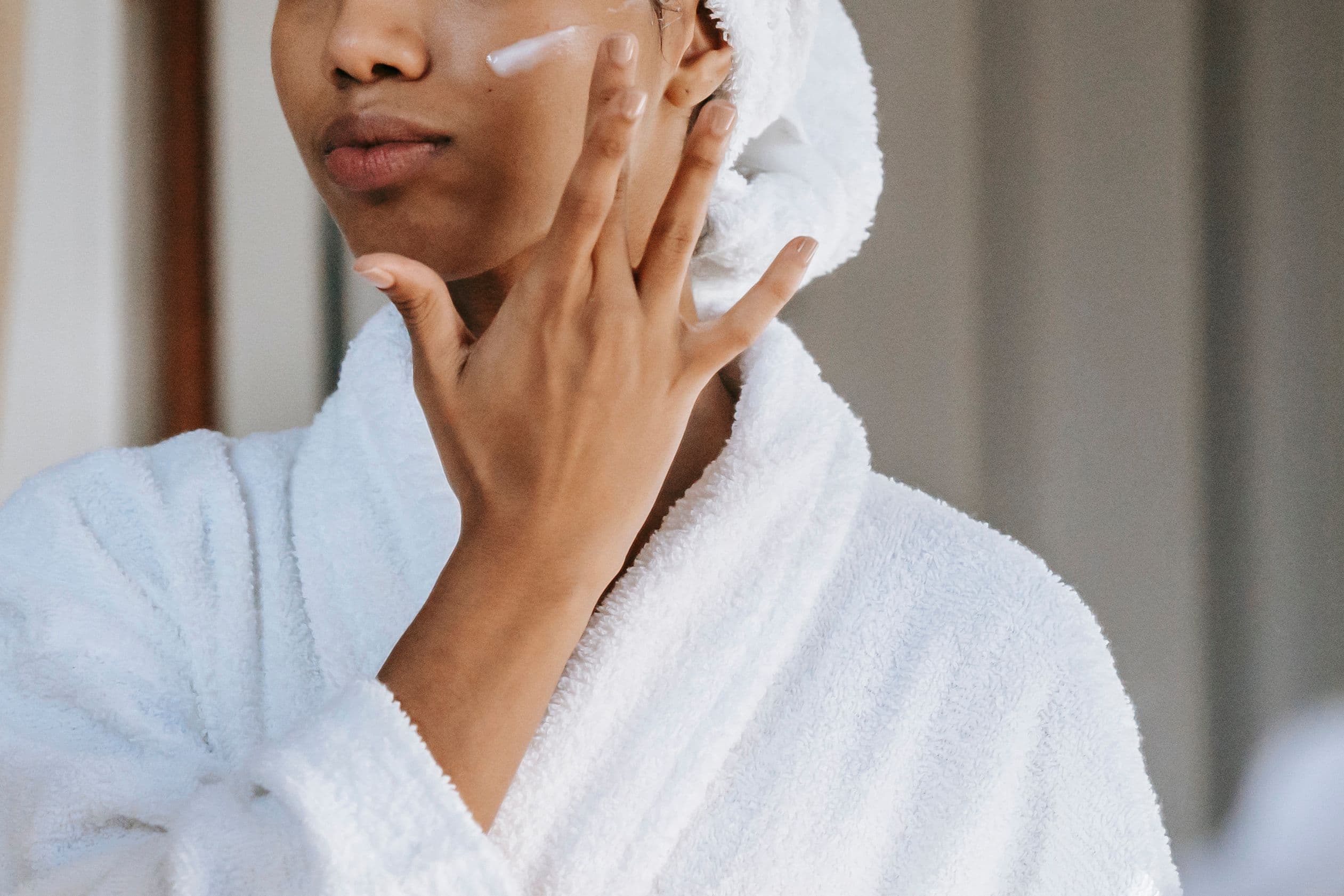 Woman applying sunscreen to her face while wearing a white robe